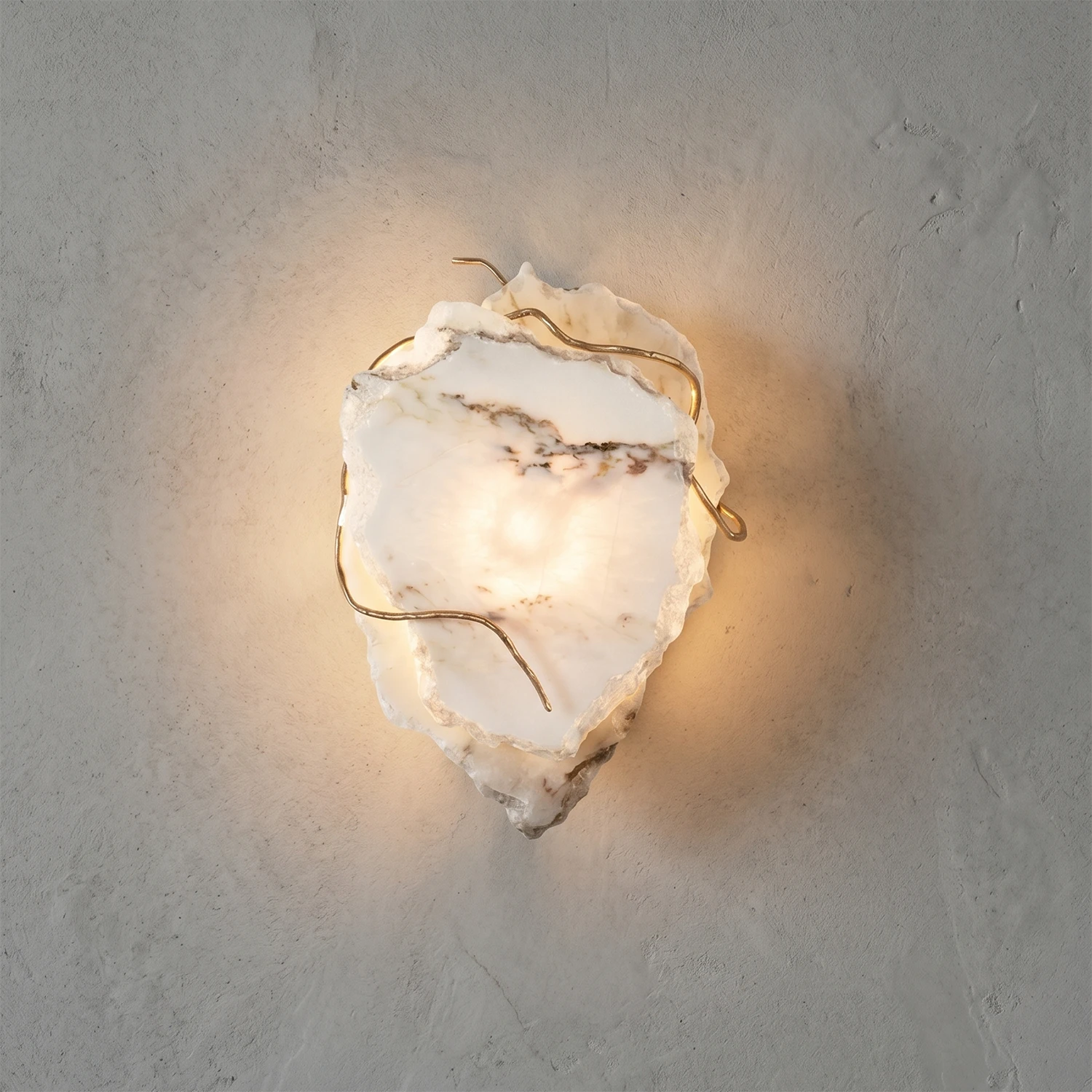Hand-carved alabaster wall sconce with warm glow, natural stone texture, and brass accents on textured wall