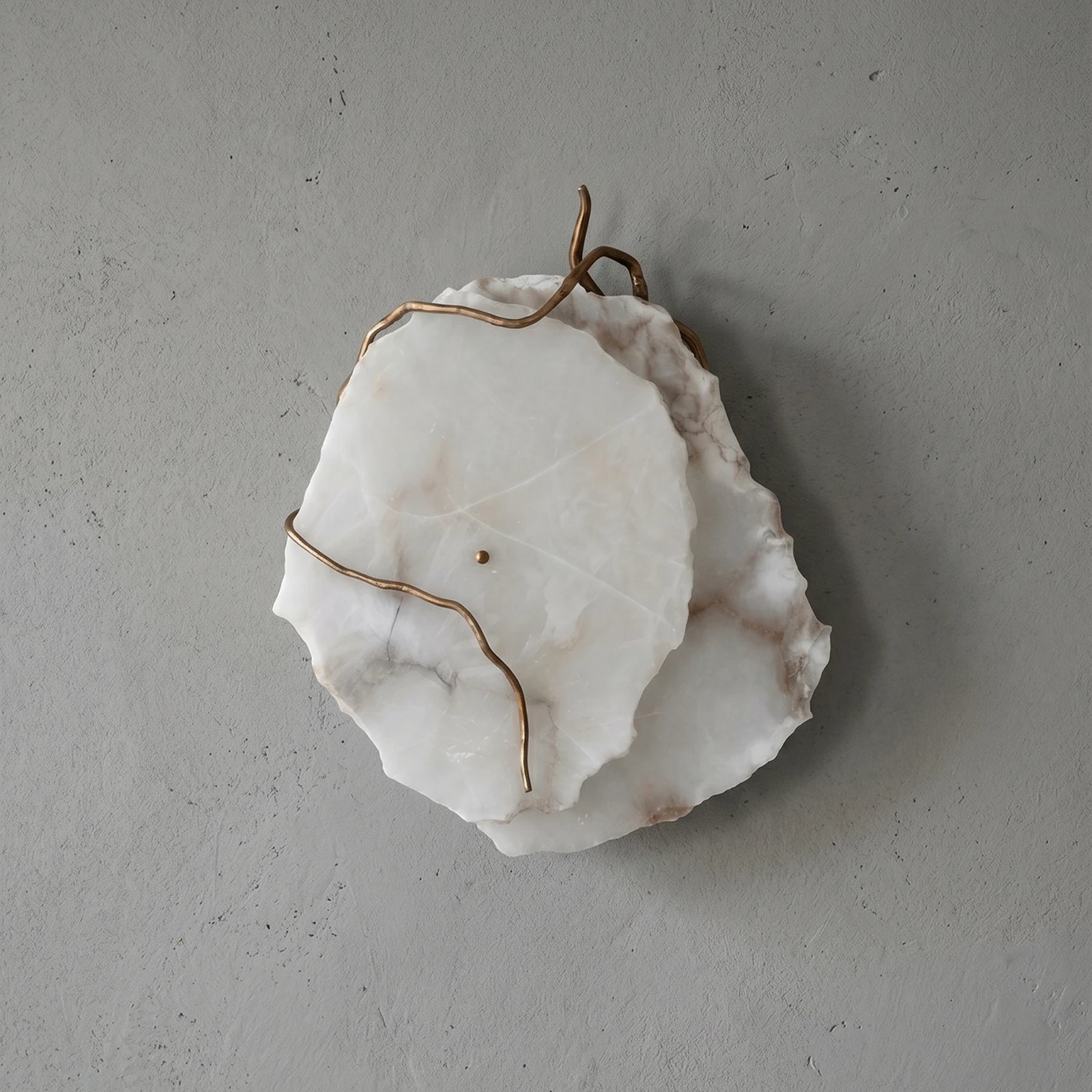 The same sconce switched off, the pale stone and brass reading as a wall sculpture in daylight.