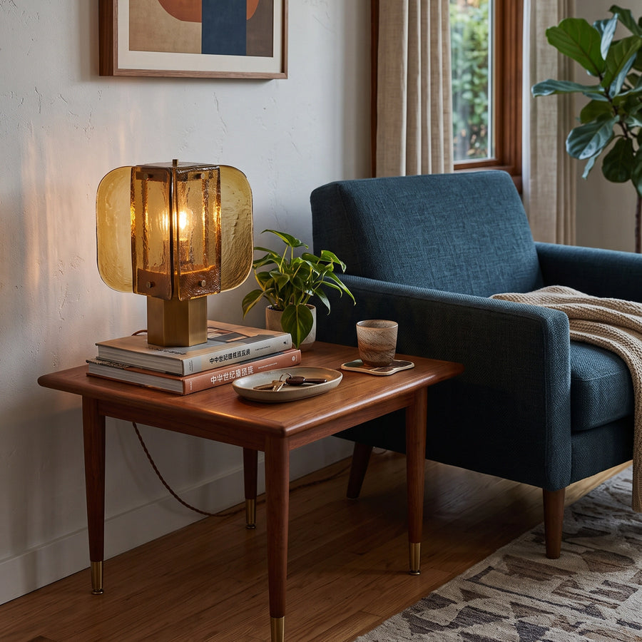 The Tramonto lamp lit on a side table beside a blue armchair.